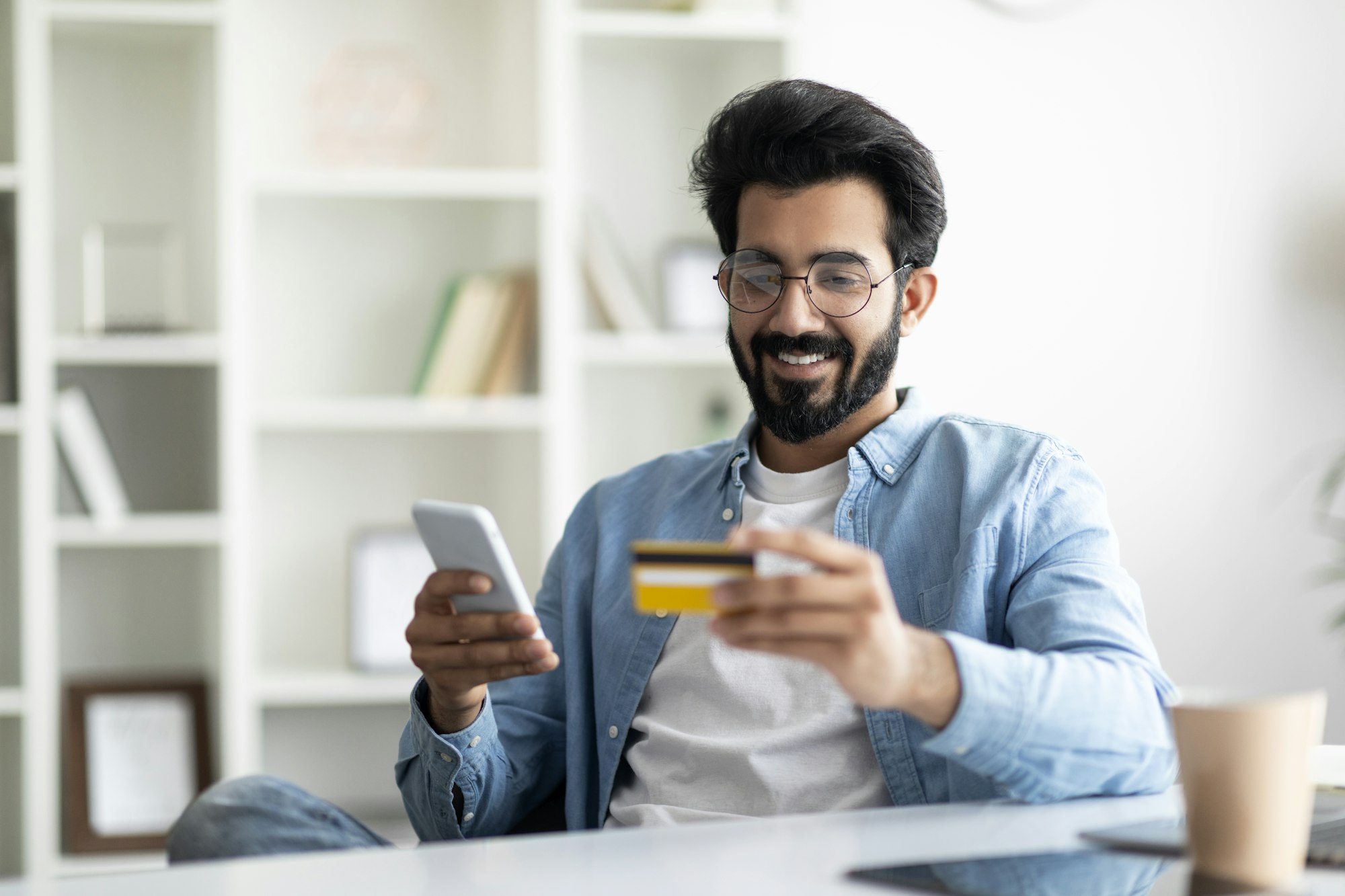 Online Loan. Portrait Of Smiling Indian Man Using Smartphone And Credit Card